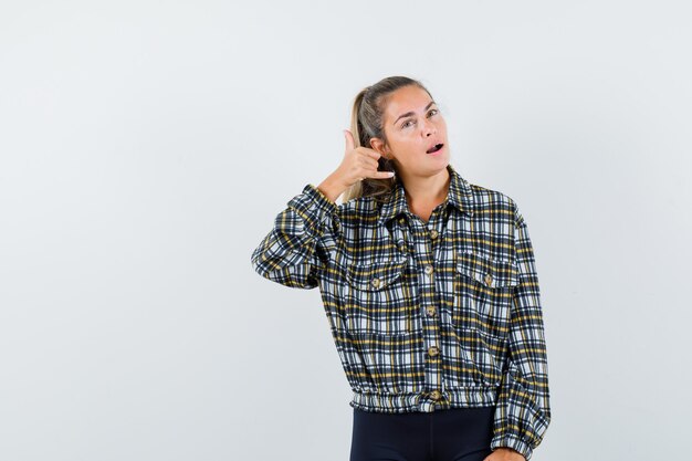 シャツ、ショートパンツで電話のジェスチャーを示し、自信を持って見える若い女性。正面図。