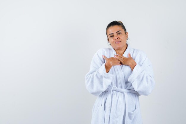 Young lady showing praying gesture in bathrobe and looking hopeful