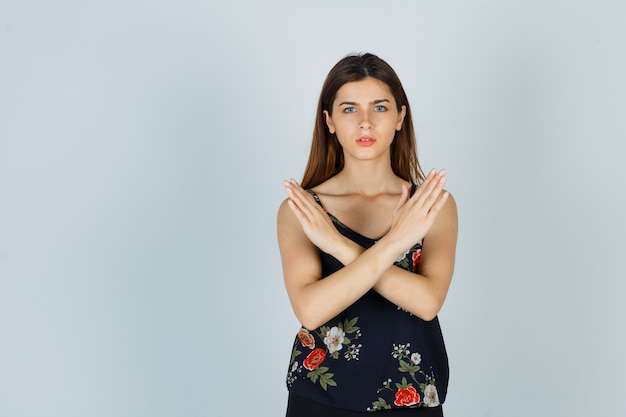 Young lady showing refusal gesture in blouse and looking serious. front view.