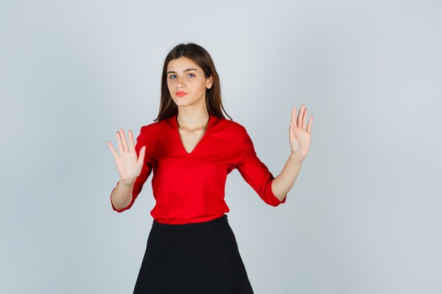 Young lady showing restriction gesture in red blouse, black skirt and looking serious