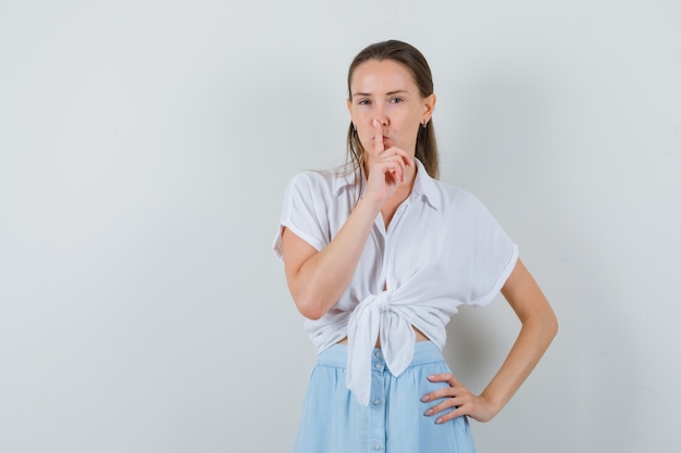Young lady showing silence gesture in blouse and skirt and looking careful
