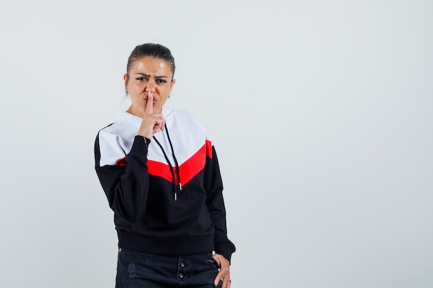 Young lady showing silence gesture in colorful sweatshirt and looking strict. front view.