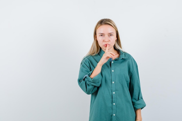 Foto gratuita giovane signora che mostra gesto di silenzio in camicia verde e sembra sensata.