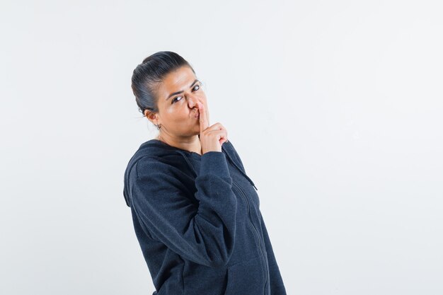 Young lady showing silence gesture in jacket and looking calm 