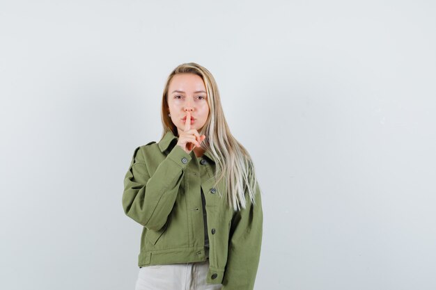 ジャケット、パンツで沈黙のジェスチャーを示し、自信を持って見える若い女性。正面図。