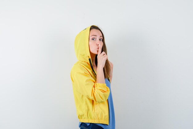 Young lady showing silence gesture in t-shirt, jacket and looking careful