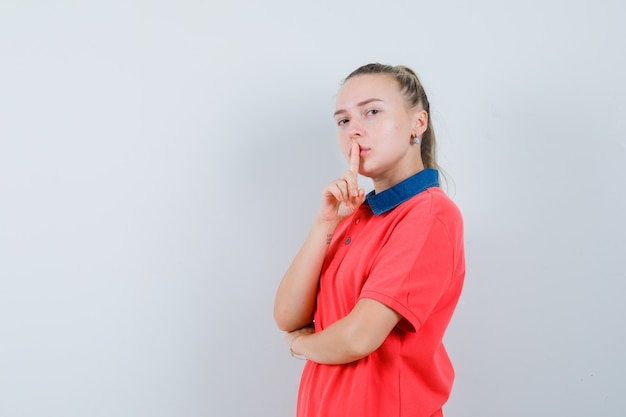 Молодая леди показывает жест молчания в футболке и смотрит осторожно