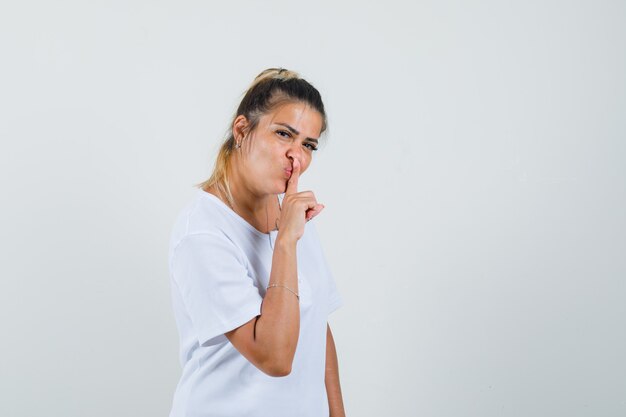 Young lady showing silence gesture in t-shirt and looking positive