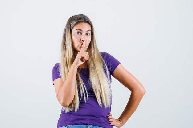 보라색 티셔츠, 청바지에 침묵 제스처를 보여주는 젊은 아가씨 조심, 전면보기.