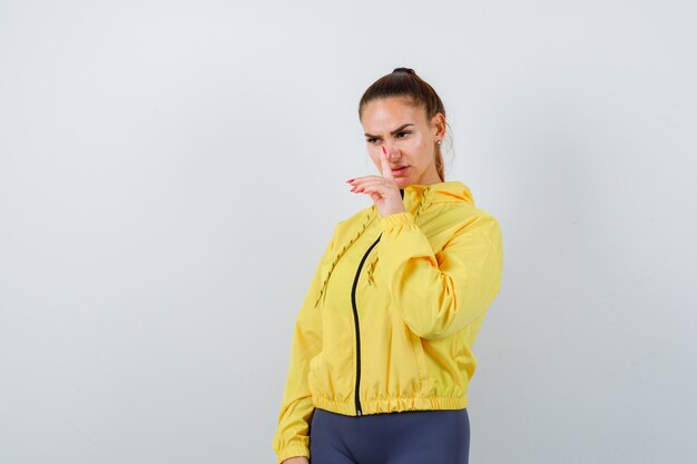 Free photo young lady showing silence gesture in yellow jacket and looking serious , front view.