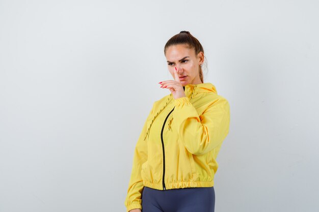 Young lady showing silence gesture in yellow jacket and looking serious , front view.