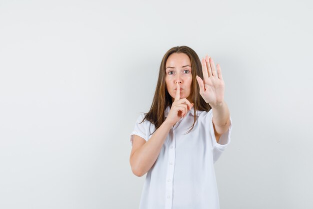 Young lady showing silence,stop gesture in white blouse and looking serious.