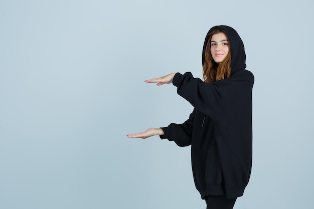 Young lady showing size sign in oversized hoodie, pants and looking confident. front view.