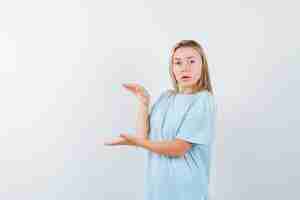 Free photo young lady showing size sign in t-shirt and looking puzzled. front view.