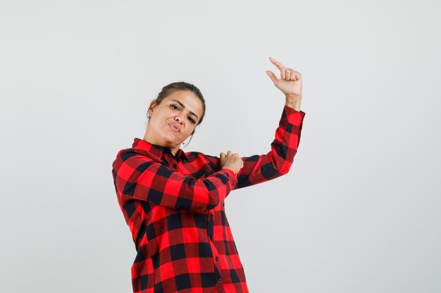 Young lady showing small size sign in checked shirt and looking confident