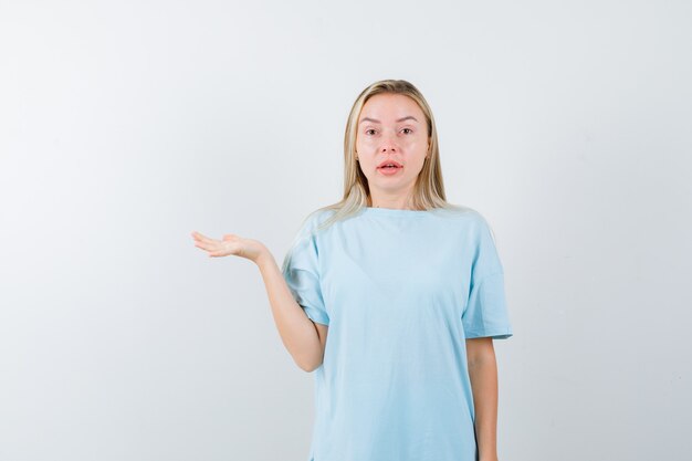 Young lady showing something in t-shirt and looking amazed. front view.