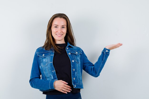 Young lady showing something or welcoming in blouse, jacket and looking confident , front view.