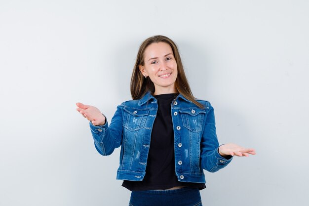 Young lady showing something or welcoming in blouse, jacket and looking merry, front view.