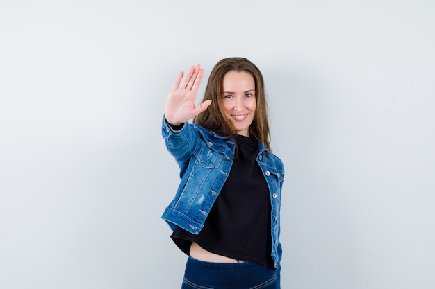 Young lady showing stop gesture in blouse, jacket and looking confident. front view.