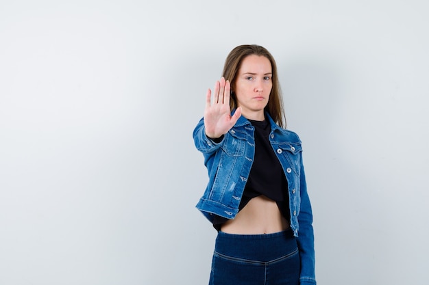 Young lady showing stop gesture in blouse and looking resolute. front view.