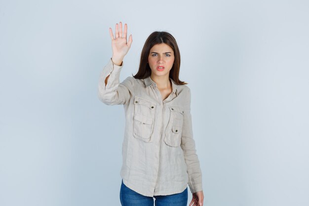 Young lady showing stop gesture in casual, jeans and looking serious. front view.