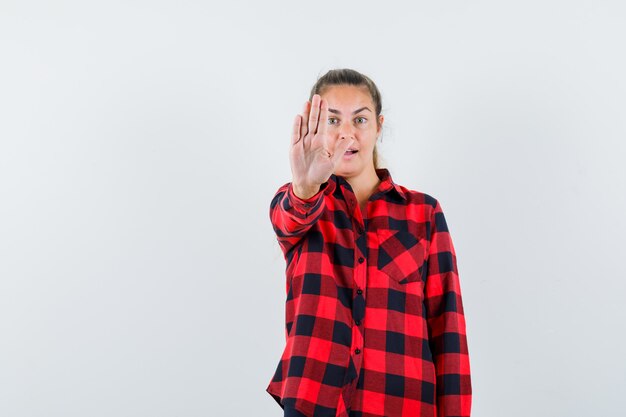 Young lady showing stop gesture in casual shirt and looking confident. front view.