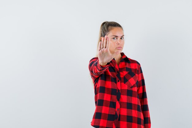 Young lady showing stop gesture in casual shirt and looking serious. front view.