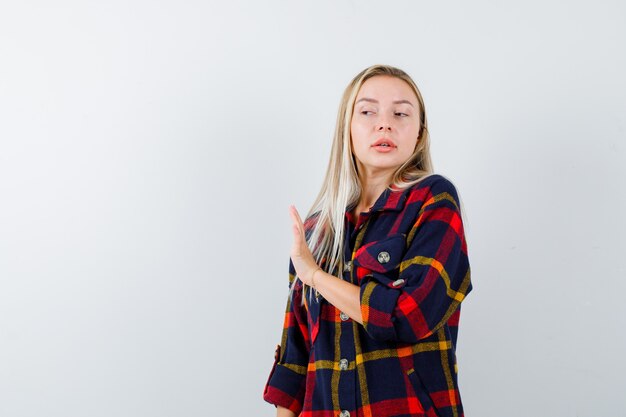 Young lady showing stop gesture in checked shirt and looking confident. front view.