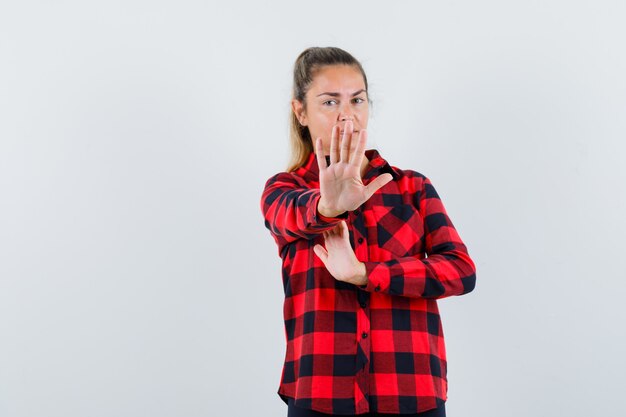 Young lady showing stop gesture in checked shirt and looking scared