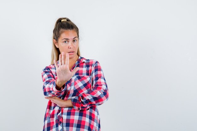 Young lady showing stop gesture in checked shirt and looking serious , front view.