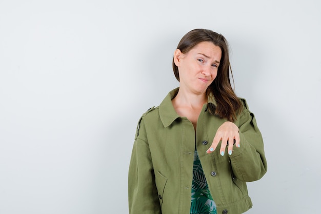 Young lady showing stop gesture in green jacket and looking displeased , front view.