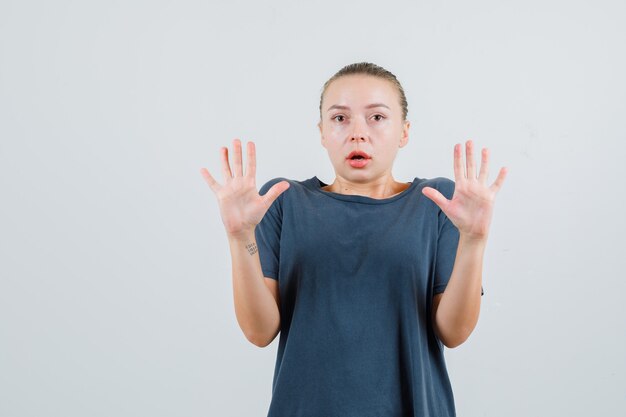 Young lady showing stop gesture in grey t-shirt and looking scared