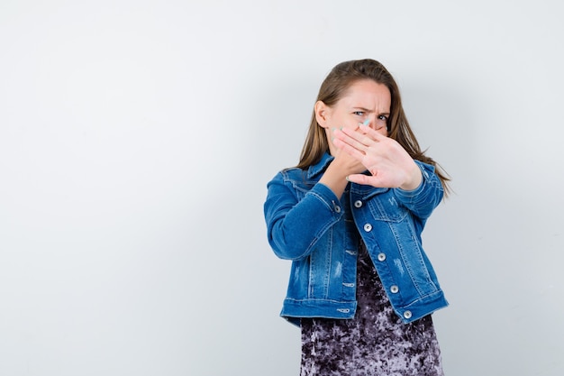 Giovane donna che mostra il gesto di arresto, tenendo la mano sulla bocca in abito, giacca di jeans e sembra disgustata. vista frontale.