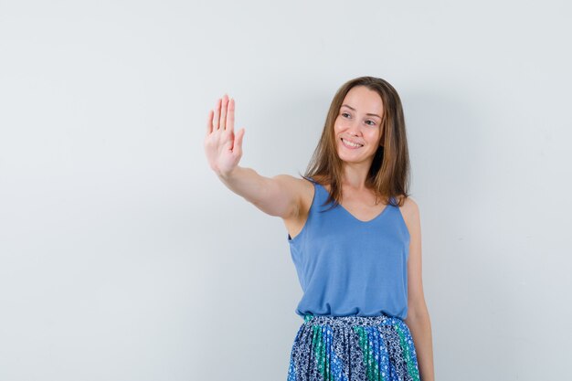 Young lady showing stop gesture in singlet, skirt and looking cheerful. front view.