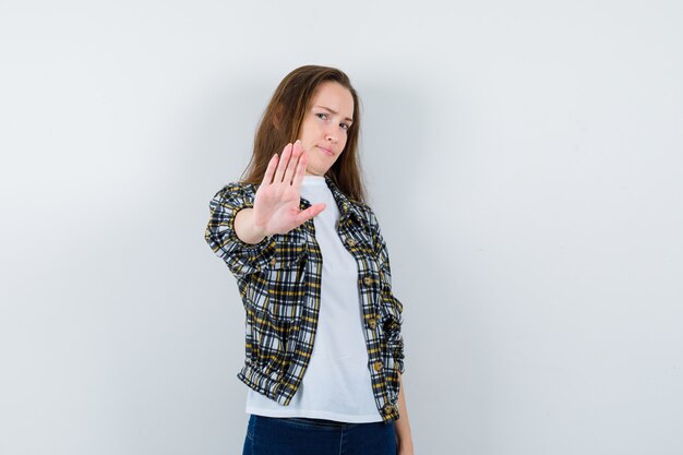 Young lady showing stop gesture in t-shirt, jacket and looking bored , front view.