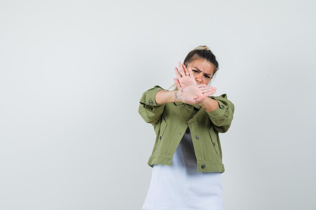 Young lady showing stop gesture in t-shirt jacket and looking irritated