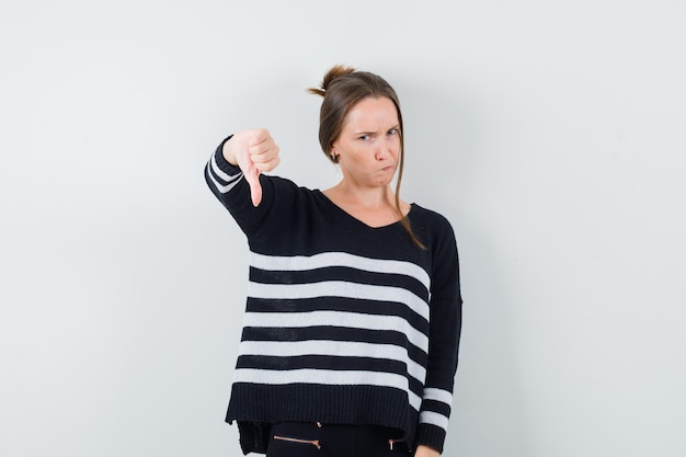 Young lady showing thumb down in casual shirt and looking discontent