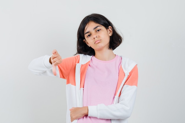 Young lady showing thumb down in jacket, pink shirt and looking displeased.