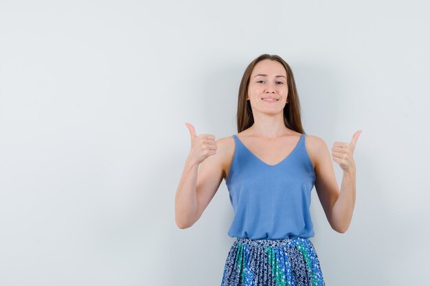 Young lady showing thumb up in blouse,skirt and looking glad , front view. space for text