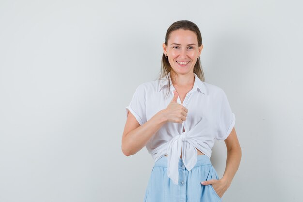 Young lady showing thumb up in blouse and skirt and looking happy