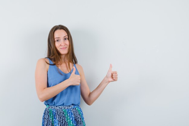 Young lady showing thumb up in blue blouse,skirt and looking optimistic. front view. space for text