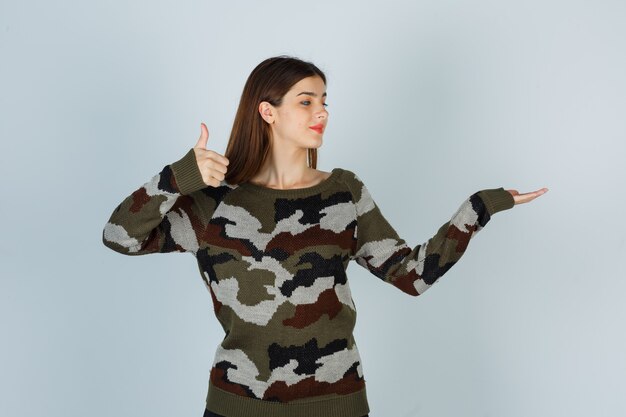 Young lady showing thumb up while pretending to show something in sweater