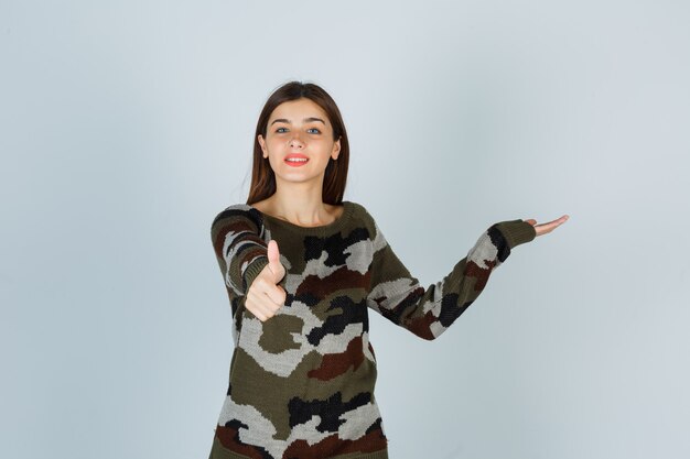 Young lady showing thumb up while pretending to show something in sweater