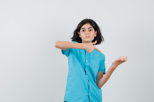 Young lady showing thumb up while raising her open palm in blue shirt and looking great.