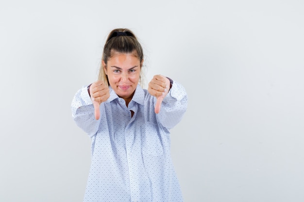 Foto gratuita giovane signora che mostra i pollici in giù in camicia e che sembra carina