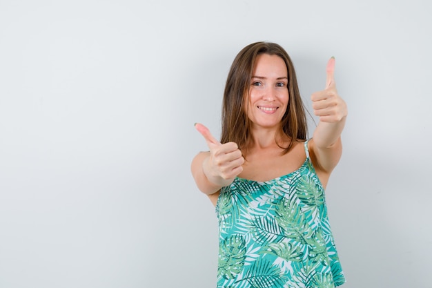 Young lady showing thumbs up in blouse and looking happy. front view.