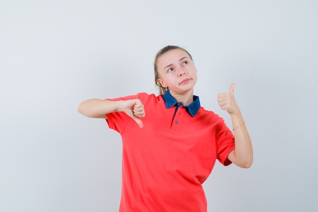 Young lady showing thumbs up and down in t-shirt and looking hesitant