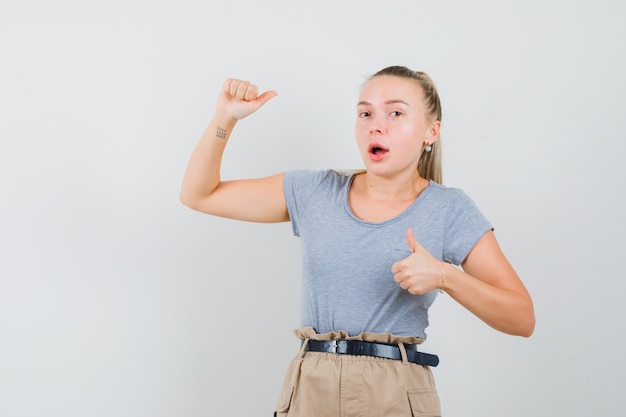 Foto gratuita giovane signora che mostra i pollici su e giù in maglietta e pantaloni e sembra sorpresa