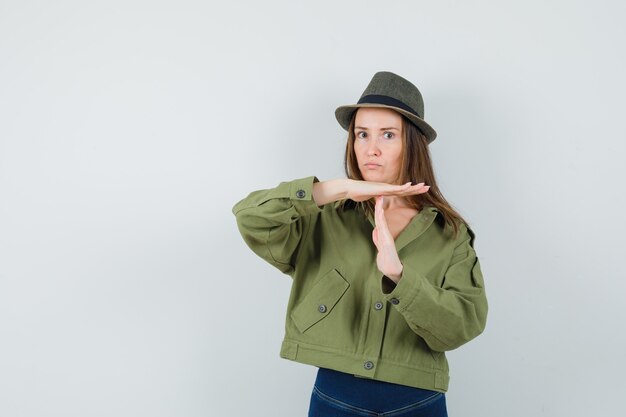 Young lady showing time break gesture in jacket pants hat and looking serious