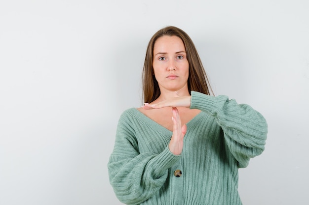 Young lady showing time break gesture in wool cardigan and looking serious. front view.